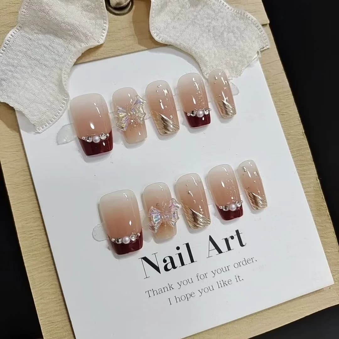 Faux ongles french tip courts avec paillettes dorées et motif nœud